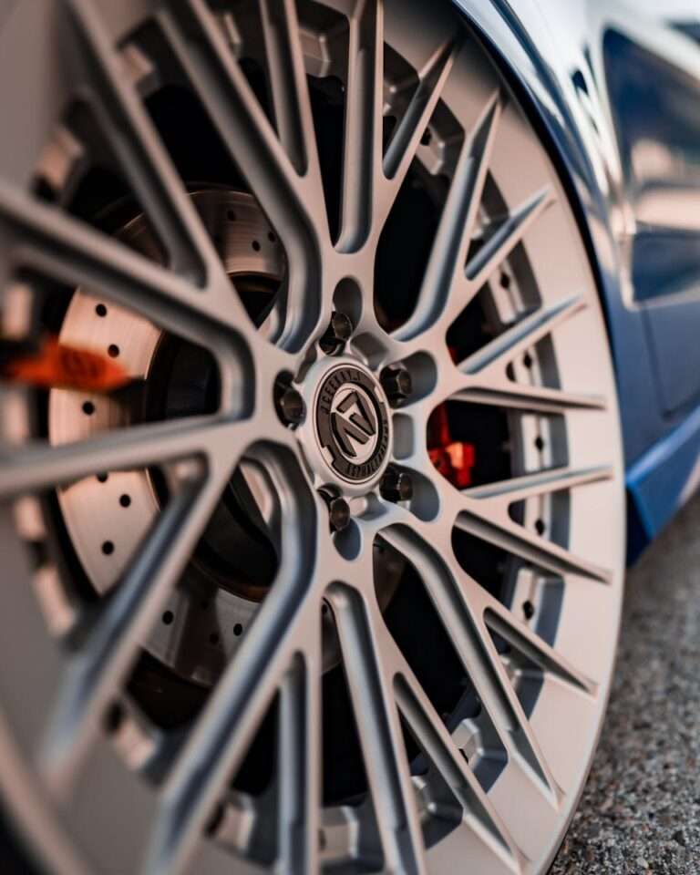 Detailed close-up of a luxury car wheel showcasing intricate chrome and aluminium design in vibrant lighting.